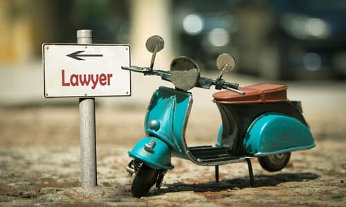 A miniature scooter motorcycle next to a sign pointing in the direction of a lawyer.