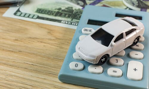 A miniature car on top of a calculator next to some scattered bank notes.