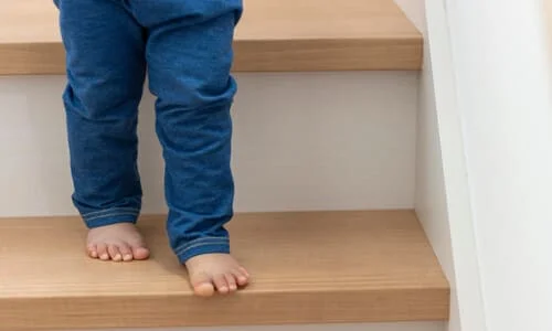An unattended toddler trying carefully to walk down a set of stairs.