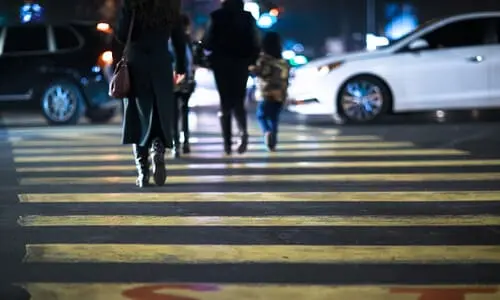A pedestrian crossing at night with several people and vehicles on it.