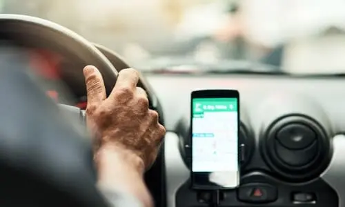 An over-the-shoulder shot of an Uber driver with the app open on his phone next to the dashboard.
