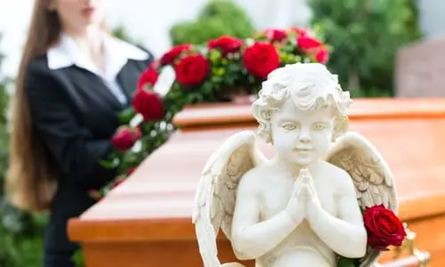 A woman mourning over a loved one's casket at a funeral, with a statue of a cherub in the foreground.