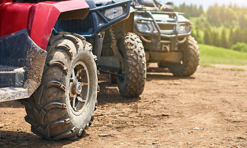 Quad bike ATVs in a single file on a dirt track.