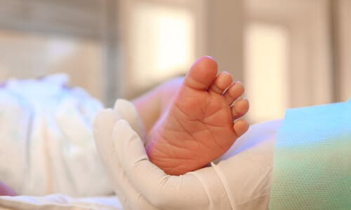 A closeup shot of a doctor's hand holding up a baby's foot to check it for injuries.