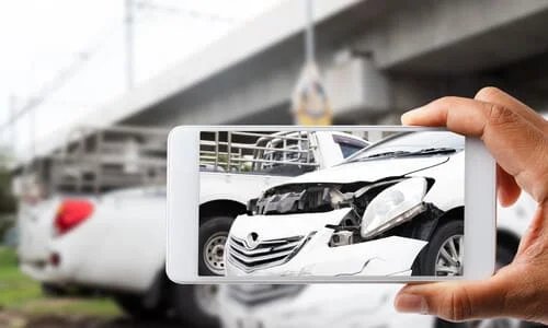A first-person view image of a person taking a photo of their car accident on their phone.