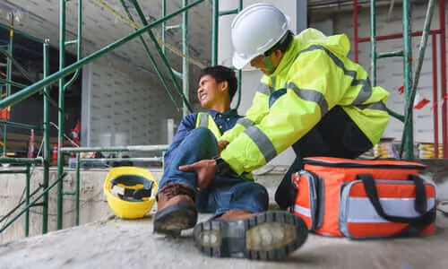 A construction worker holding a coworker's injured leg at a construction site.