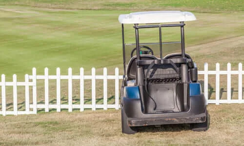 A worn-out golf cart parked next to a fence on a golf course.