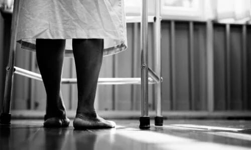 A black and white image of an elderly person's legs behind a walker.
