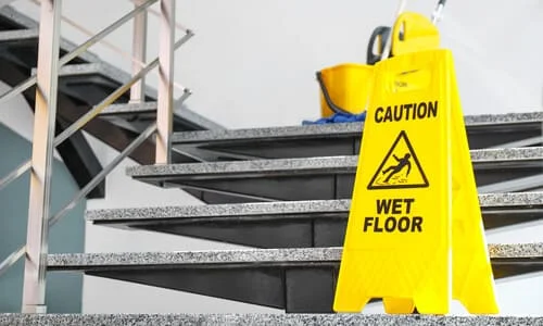 A yellow wet floor caution sign and mop bucket on an outdoor staircase.