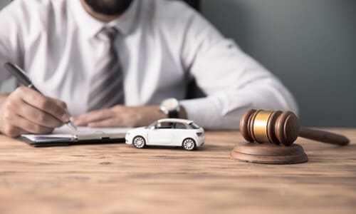 A car accident lawyer filling out forms for a client, with a miniature car on his desk next to a gavel.