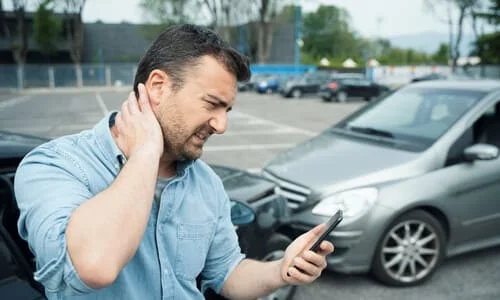 A man grasping his neck in pain while calling for help after a collision between his car and another vehicle.