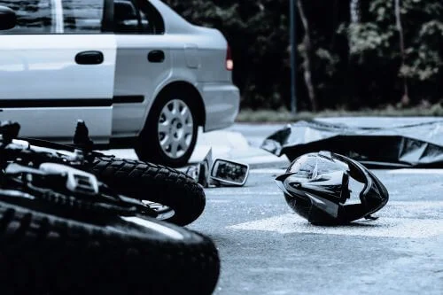 A motorcycle is laying on its side after an accident with a silver car.