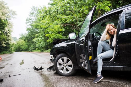 A worried young woman in a black SUV calls for help on her cell phone after a car accident.