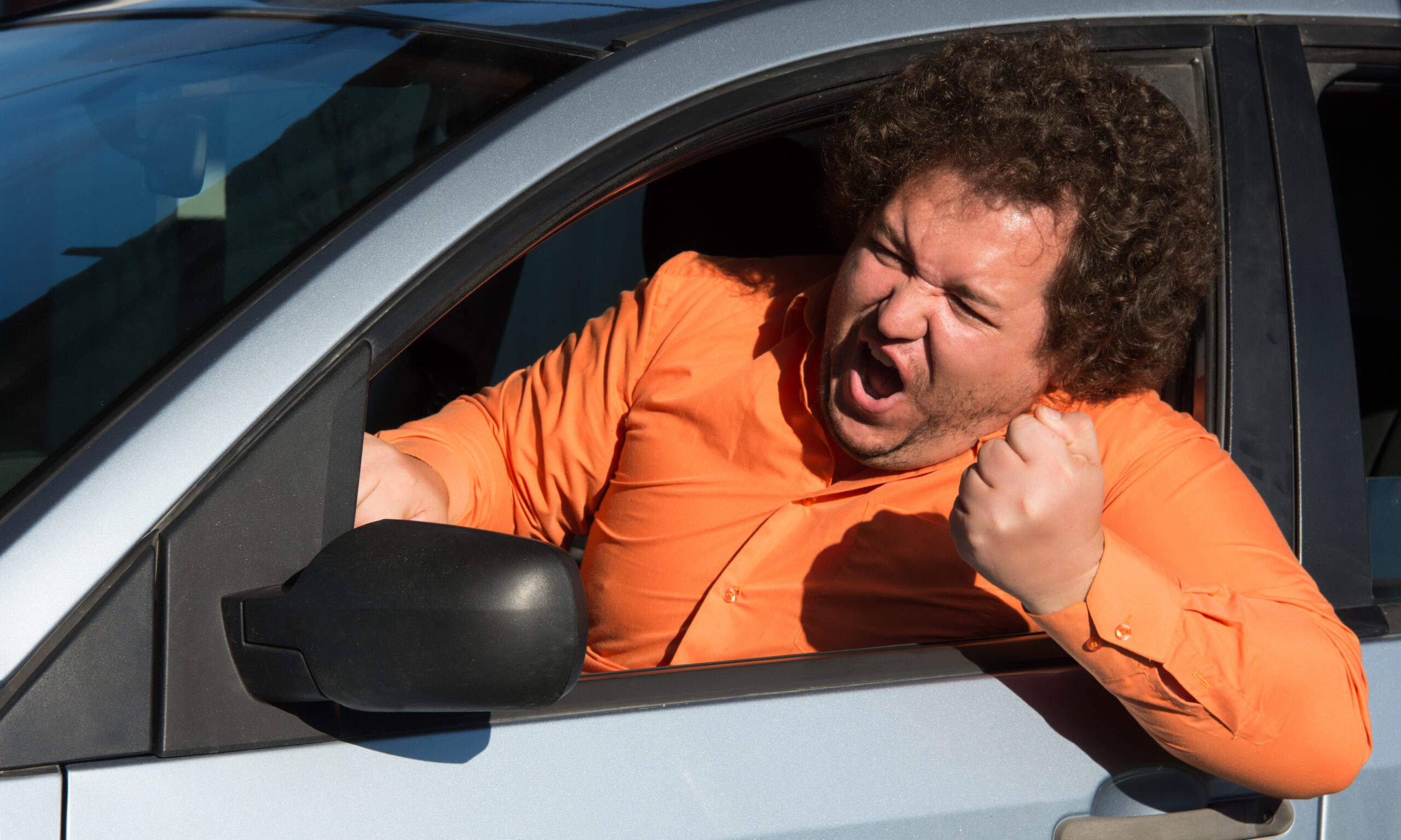 An angry driver yelling out of the side of his window at another vehicle on the road.