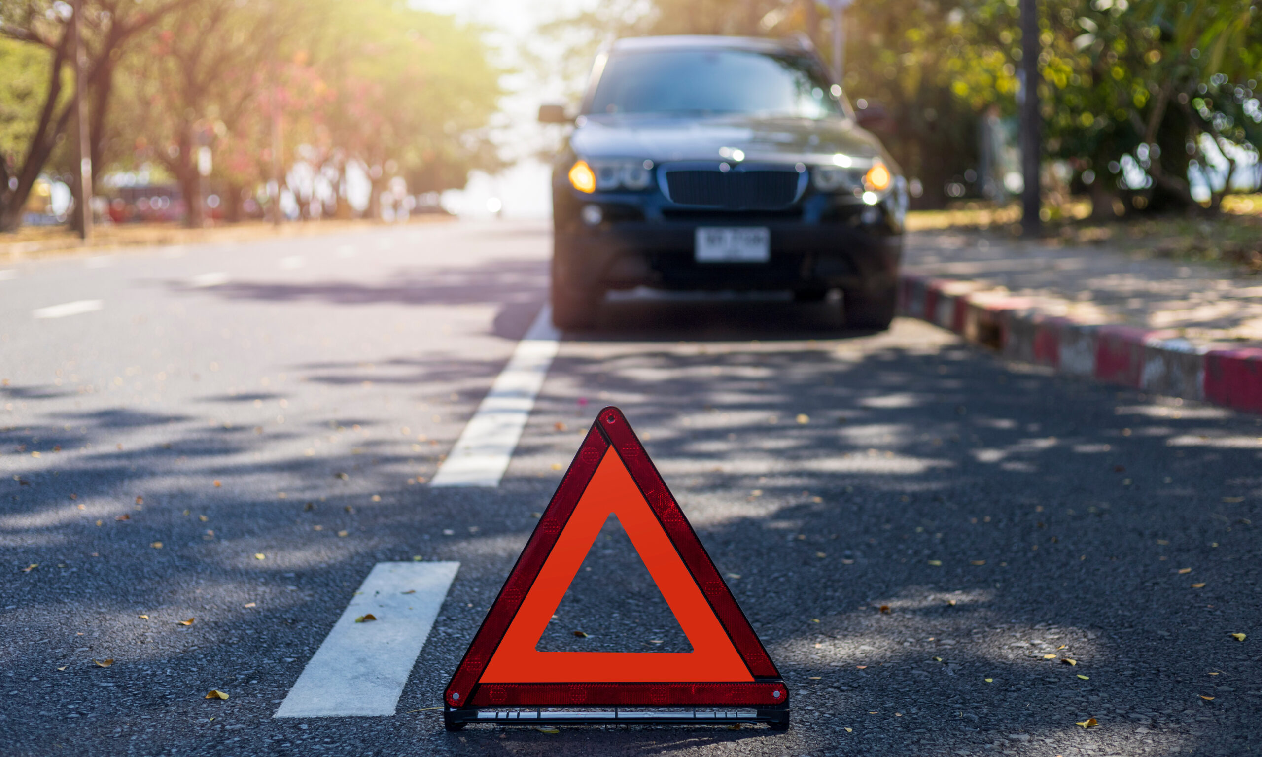 A car stopped on the side of a suburban road behind an early warning device.