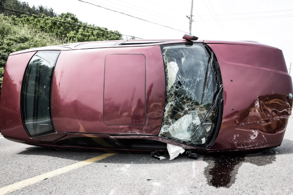 A maroon car lying on its side after a serious car accident on the road.