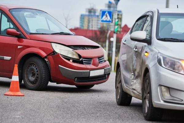 A red car and a grey car stopped after a traffic collision on an urban road.