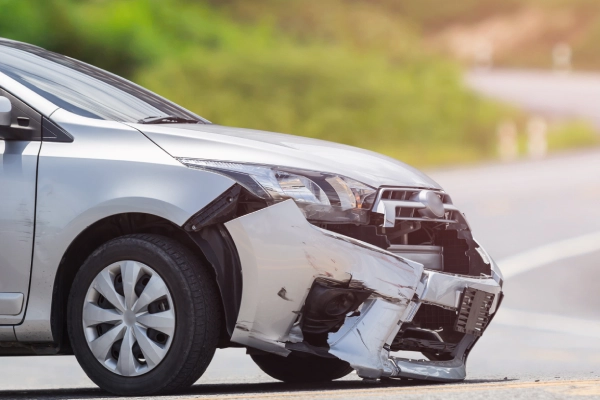 A silver-grey car with a damaged and broken front bumper after a daytime car accident.