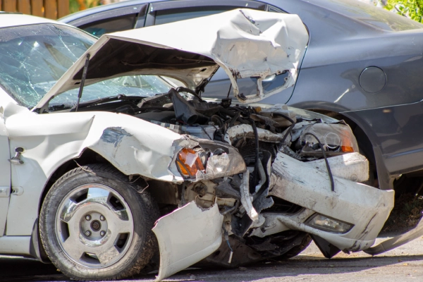 A white car totaled after a car accident and stopped on the road next to a dark blue one.