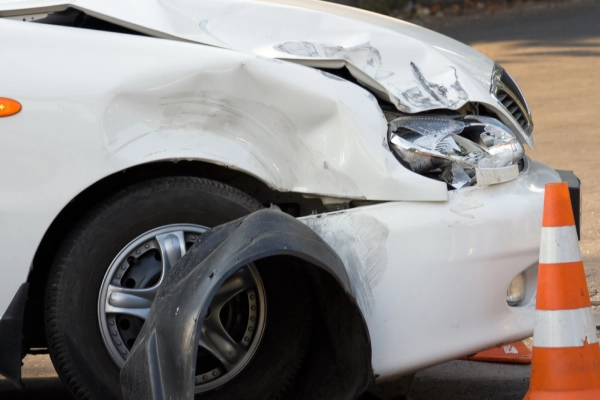 A white car parked behind a traffic cone and waiting for assistance after a car accident.