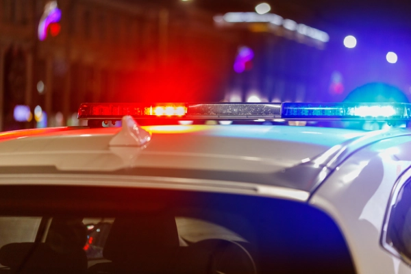 Red and blue flashing lights of a white police car in a depth of field shot of a city at night.