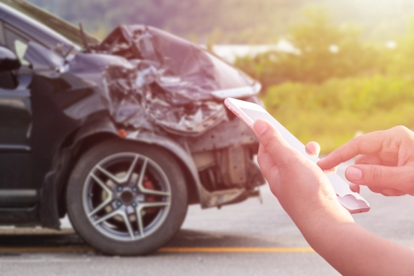 A driver calling for help on her phone after a car accident involving her black car.