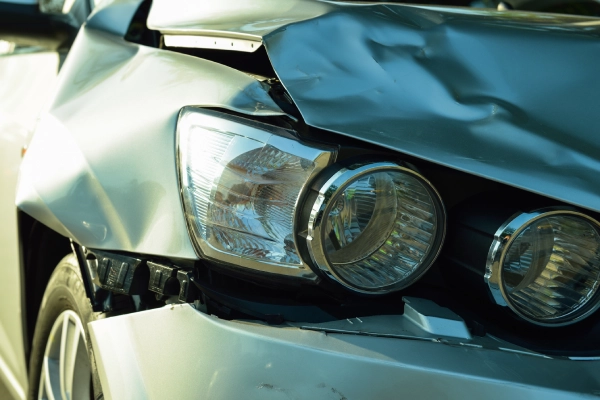 An angled shot of a silver car's crumpled front end displaying headlights damaged in an accident.