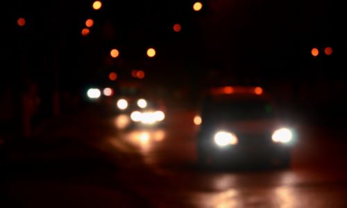 A depth of field shot of cars driving along a main road in a city at night.