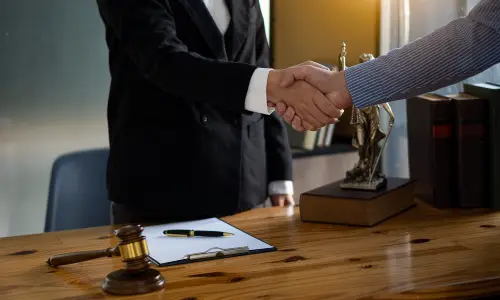 A car accident lawyer and a client shaking hands after agreeing to pursue a claim together.