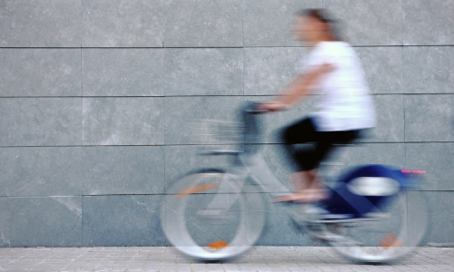 A motion-blurred shot of a cyclist driving on a street next to a high wall.