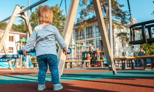 A toddler at a daycare center's playground about to use the equipment.