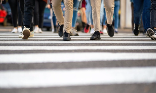 A low shot of people's feet going across a road on a white crosswalk.