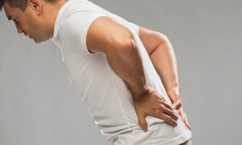 A man in a white shirt holding his back because of pain caused by a spinal injury.