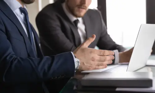 Two business professionals in suits reviewing and signing documents at a boardroom table, from the dealing with insurance series.