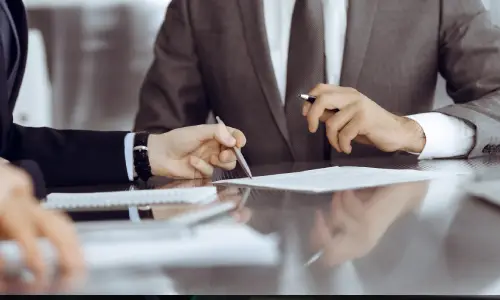 Close-up of two men in formal attire discussing details on a laptop screen, from the dealing with insurance series.