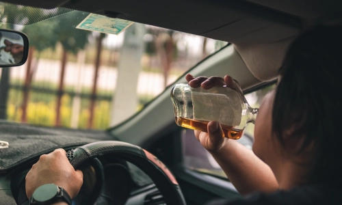 A man is drinking alcohol while driving a car.
