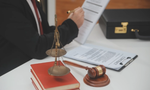 A lawyer reviewing legal documents with a brass scale and a gravel hammer on a desk.