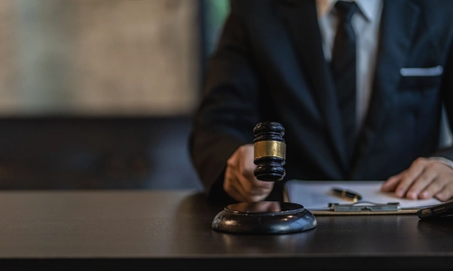 A man holding a gavel in his right hand while resting his left hand on documents on the table.