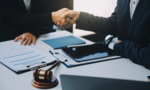 A photo of two men shaking hands with a hammer prominently in focus before them.