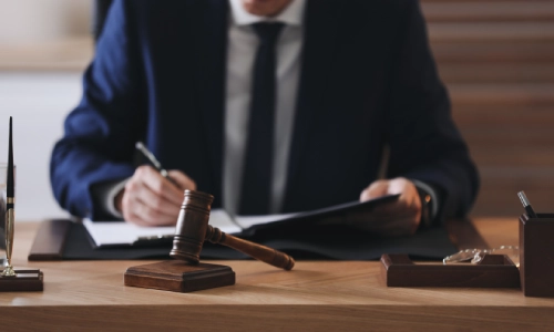 A lawyer writing notes with a gavel hammer at the foreground.